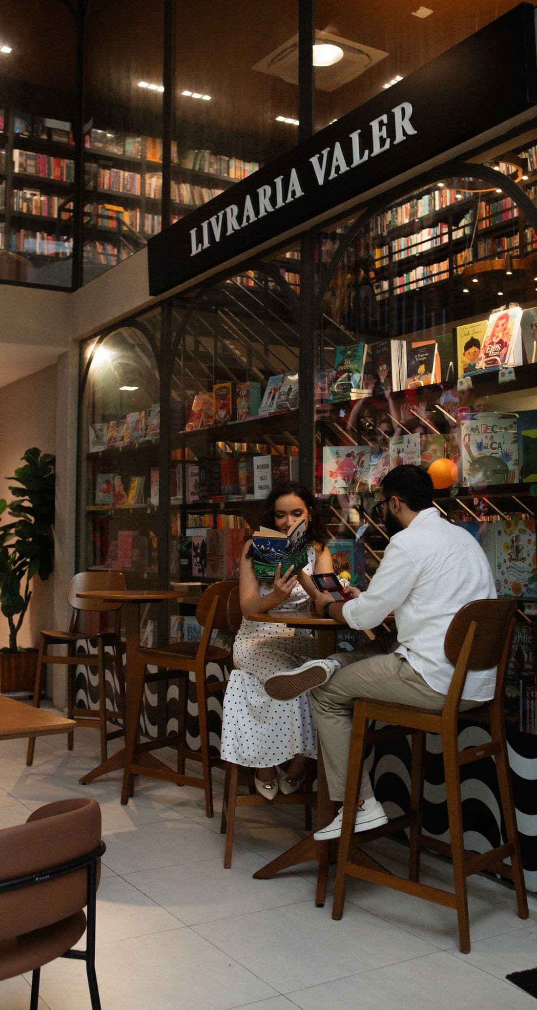 Geovanna lendo um livro e Gabriel jogando videogame em uma livraria