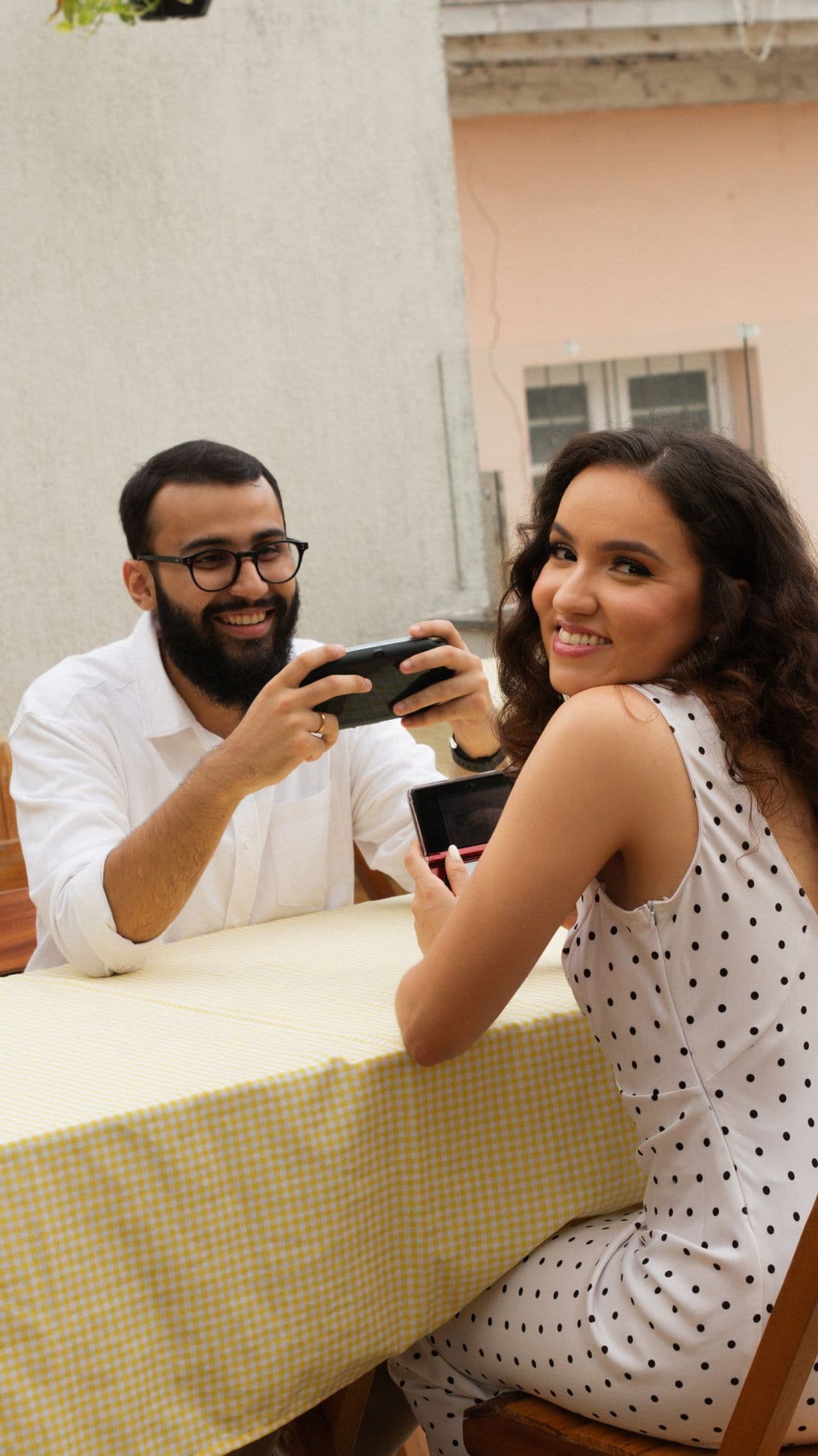 Gabriel e Geovanna jogando videogame portátil numa mesa com toalha xadrez amarela